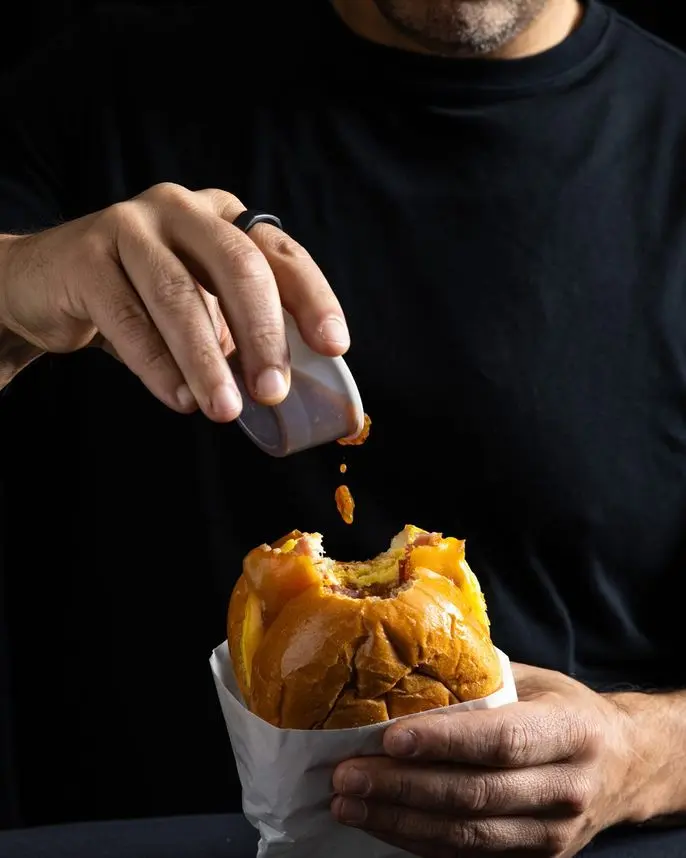 Chef Dan Figone adding signature hot sauce to a Handheld Catering brioche burger