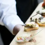 Server presenting a wooden board of appetizers, Handheld Catering is hiring drivers and servers