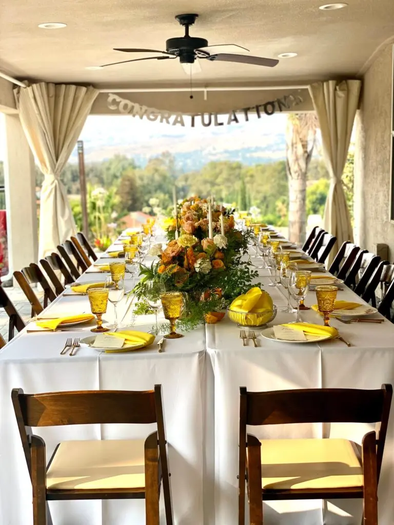 Long banquet table with yellow linens and floral centerpieces set for a San Jose private event