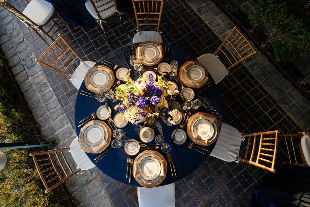 Overhead view of a formal round dinner table with floral centerpiece, gold chargers, and place settings at a private leadership dinner catered by Handheld Catering