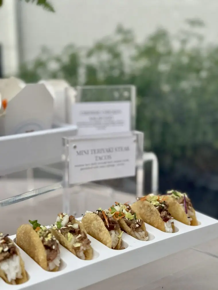 Handheld Catering baby shower tray of mini teriyaki steak tacos assembled on site, served with a printed acrylic menu card