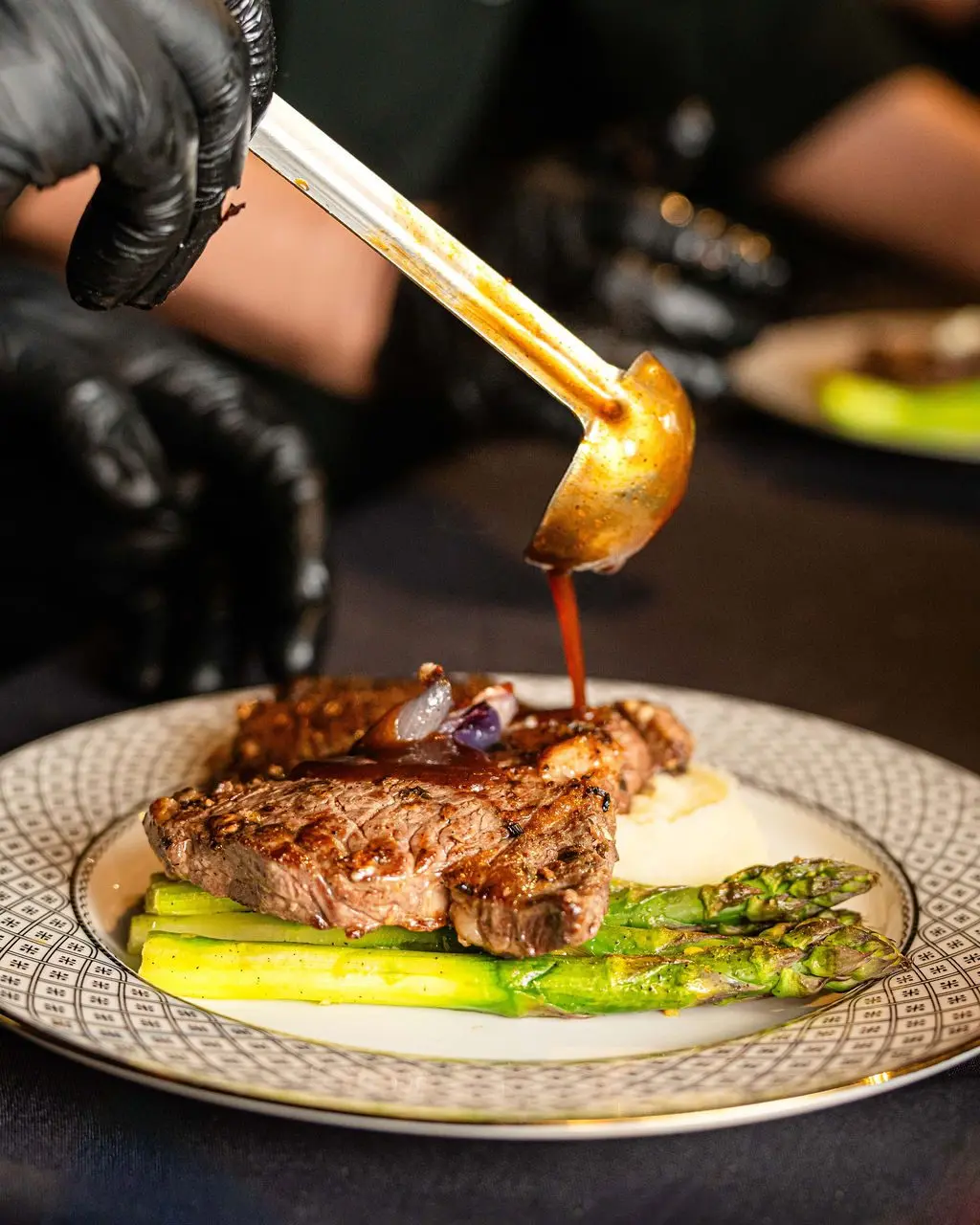 A plated roasted black Angus ribeye with demi glace, roasted garlic mashed potatoes, and charred asparagus at a private leadership dinner catered by Handheld Catering