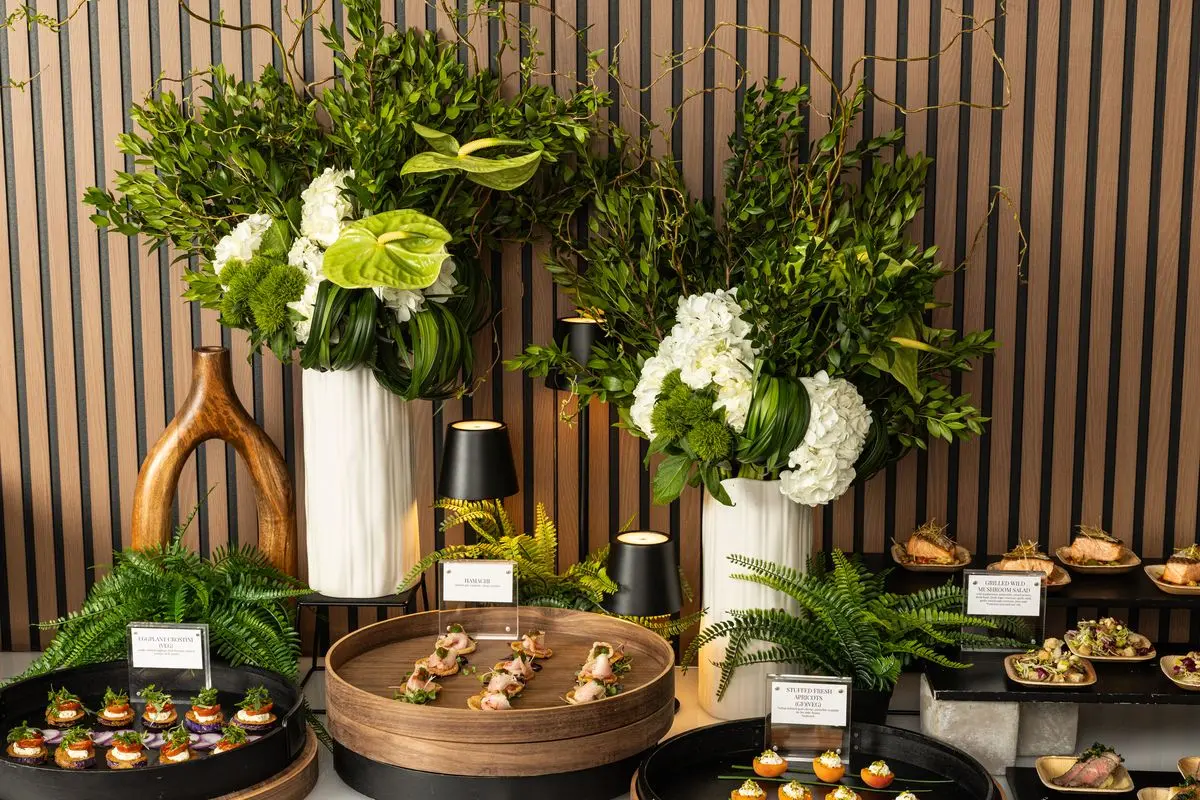 Handheld Catering small bites station set on tiered trays with florals and labeled cards for eggplant crostini, hamachi and stuffed fresh apricots