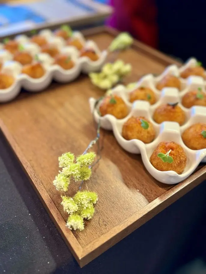 Golden arancini balls served in ceramic egg cups with delicate flowers at a birthday event