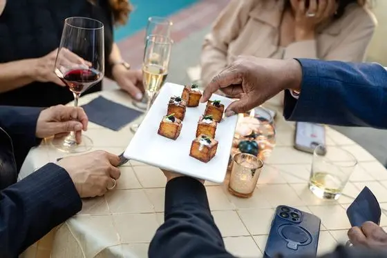 A server presenting passed mille-feuille potato appetizers to seated guests holding champagne and wine at a private dinner catered by Handheld Catering