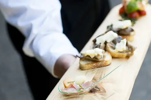 Server presenting a wooden board of appetizers, Handheld Catering is hiring drivers and servers