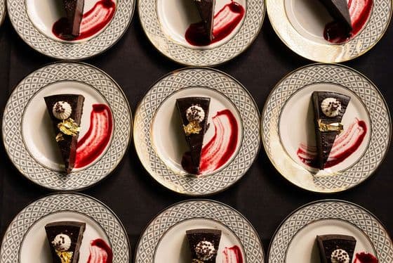 Rows of plated flourless chocolate torte finished with edible gold leaf and raspberry sauce at a private university leadership dinner catered by Handheld Catering