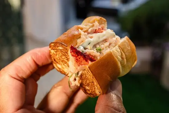 A passed lobster roll bite appetizer on a milk bun served at a backyard wedding by Handheld Catering
