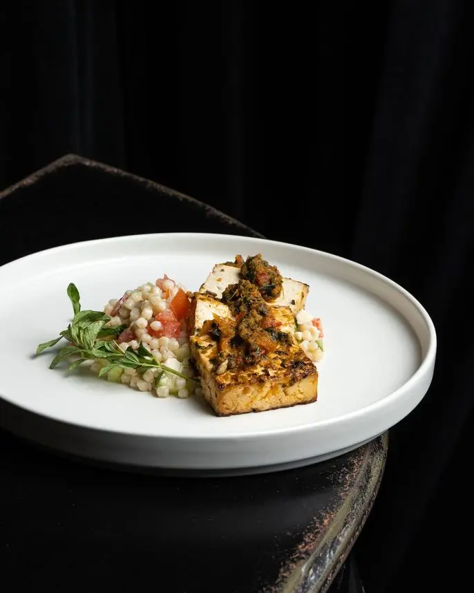 Plated herb-marinated tofu with couscous salad and fresh herbs at a Handheld Catering event