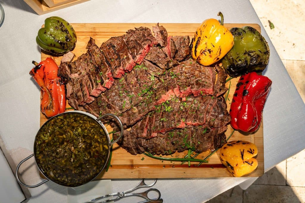 Grilled certified Angus flank steak sliced on a board with chimichurri and grilled peppers at a Monte Sereno backyard wedding, catered by Handheld Catering