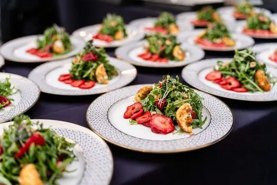 Plated arugula salads with peppered strawberries, goat cheese fritter, and micro greens on a formal table at a private plated dinner by Handheld Catering