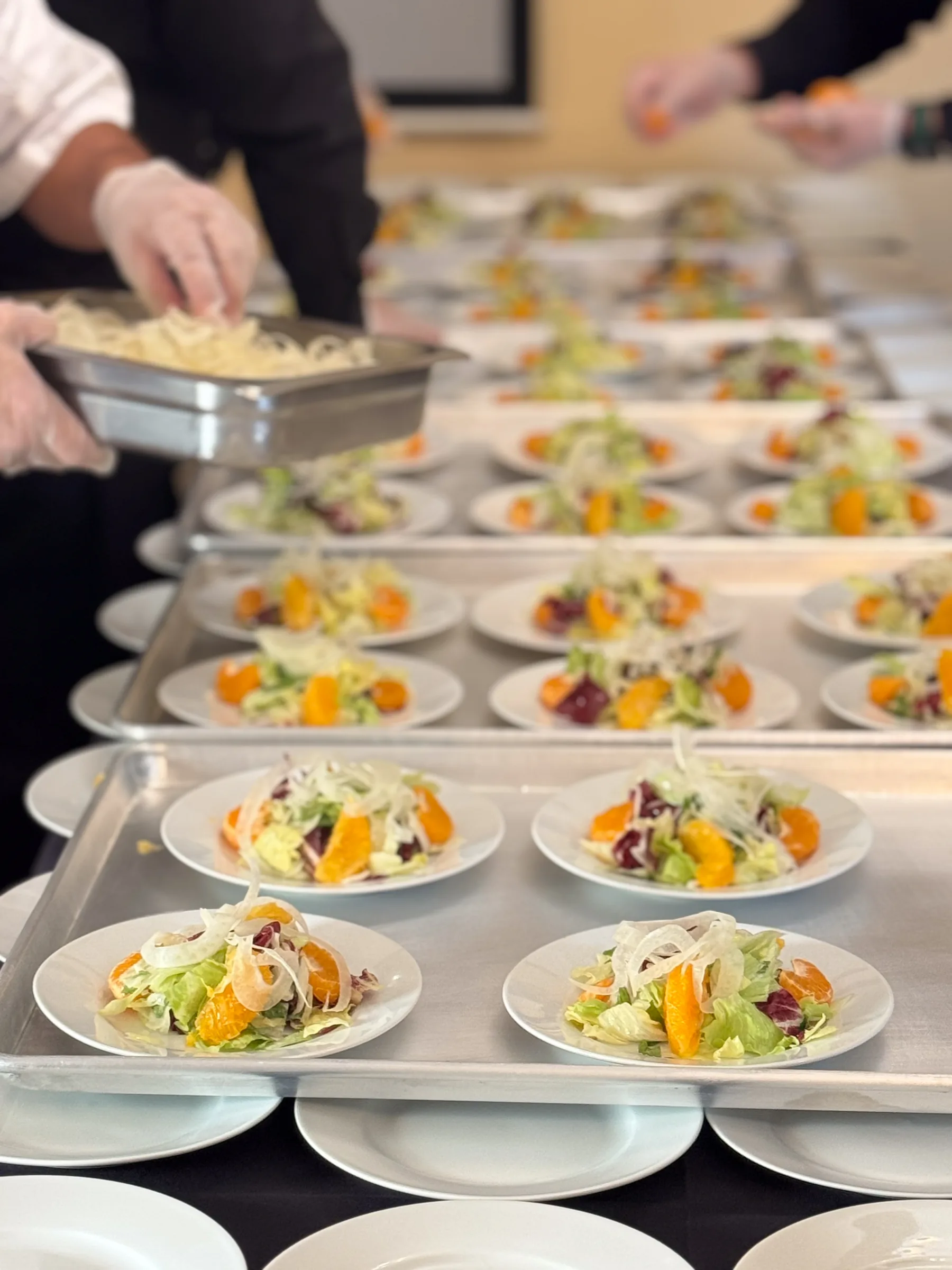 Handheld Catering kitchen team simultaneously plating mixed greens salad courses for 230 guests at the History Park San Jose fundraising gala