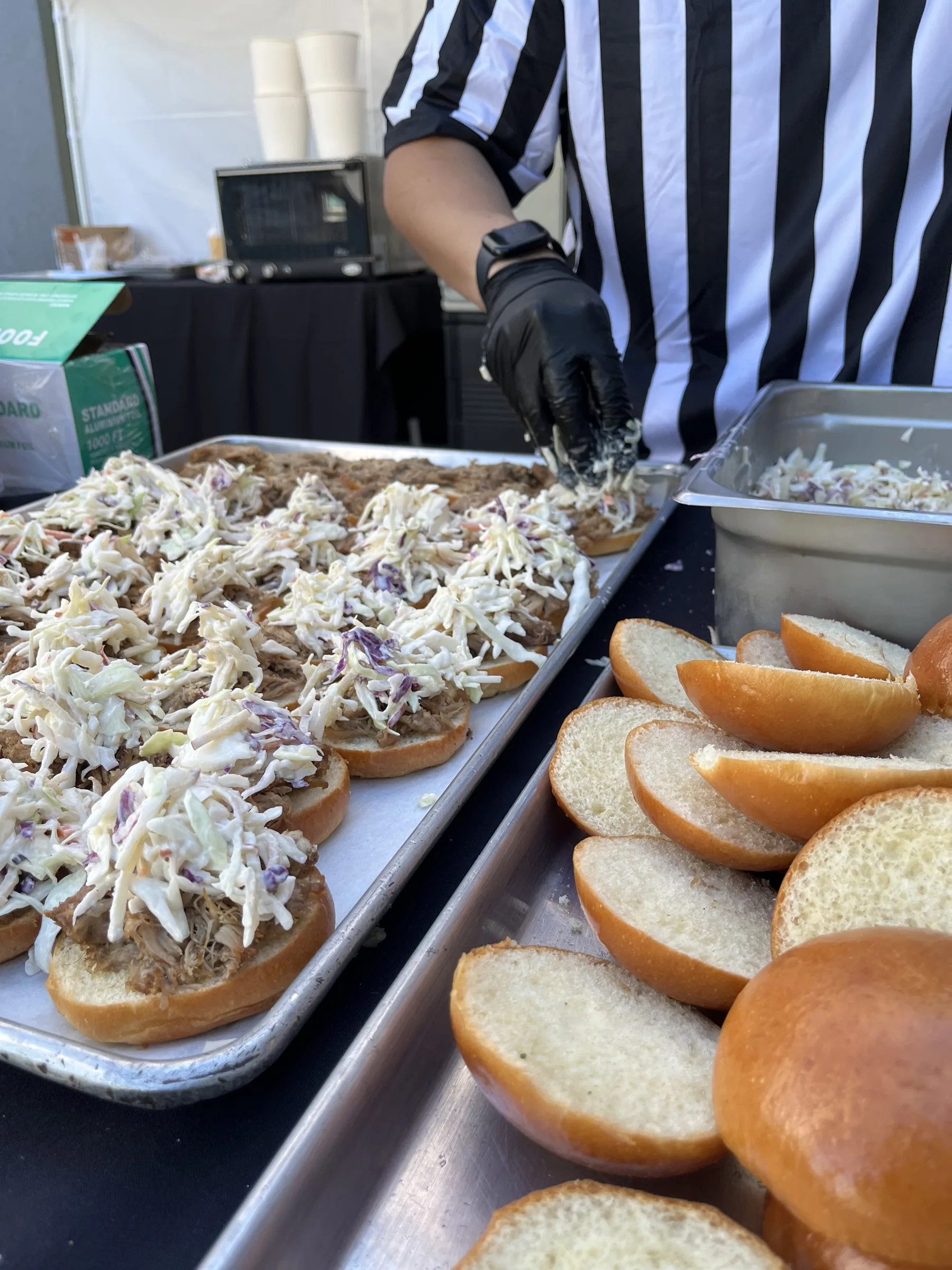 Referee-uniformed Handheld Catering team assembling pulled pork sliders with apple coleslaw for corporate tailgate buffet at Silicon Valley campus