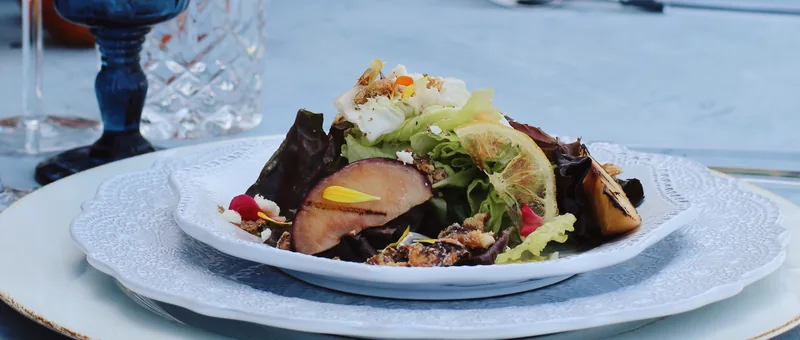 Grilled stone fruit and Bibb salad served family-style at an outdoor wedding by Handheld Catering