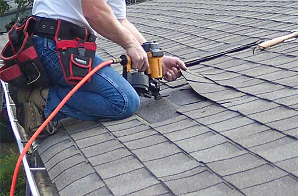 Man on roof of a home, holding a nailing gun.