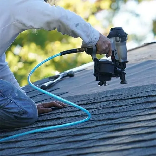 Man on roof of a home, holding a nailing gun during home shingle installation.