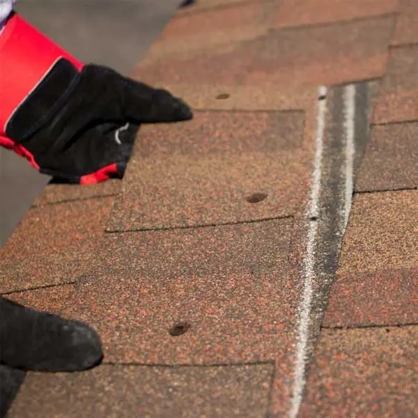 Man wearing gloves and stripping shingles off of a roof.