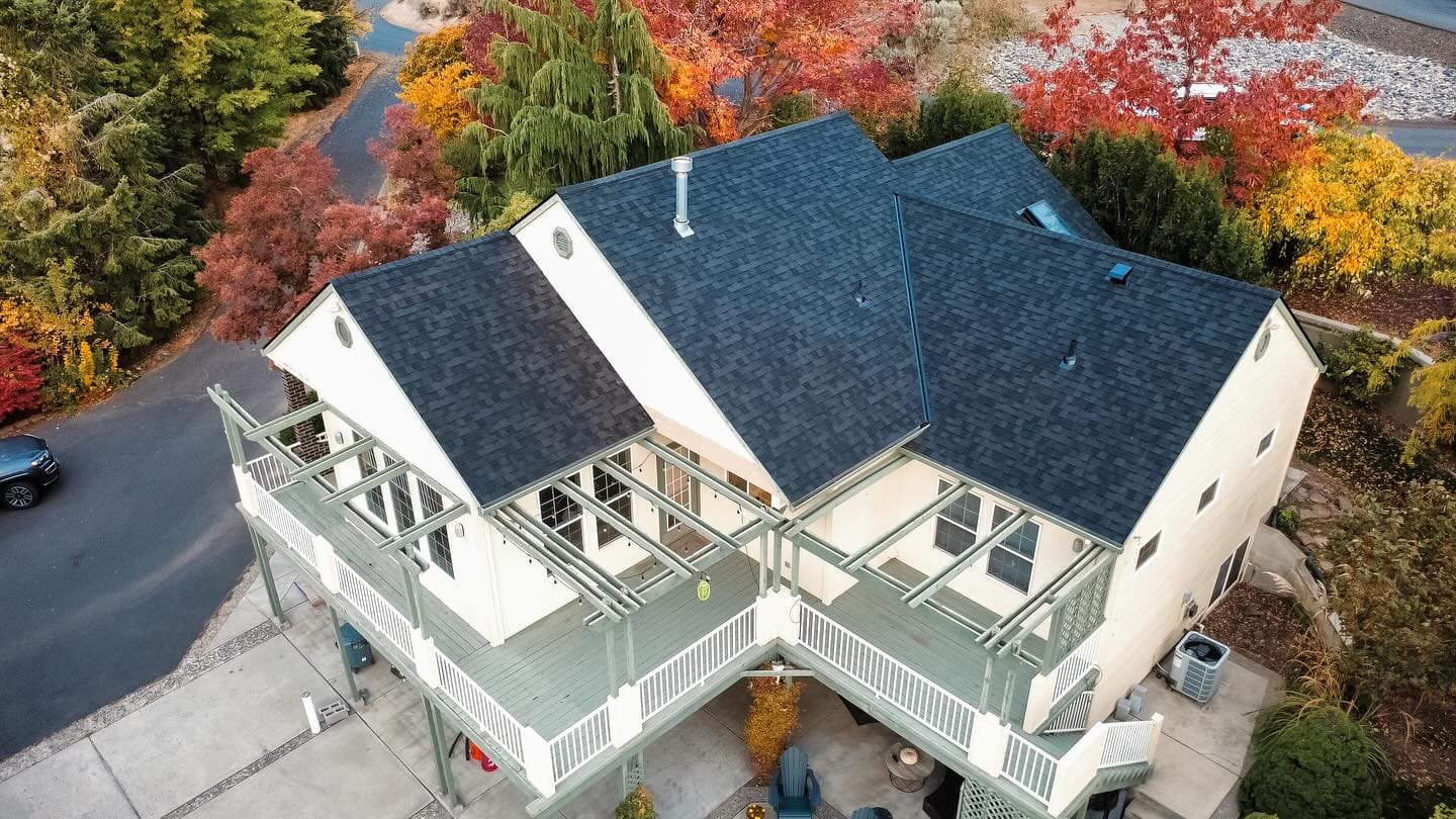Big house with dark shingle roof surrounded by fall foliage