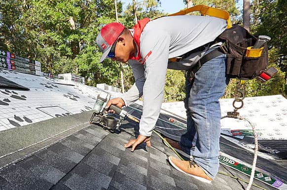 Man on roof of a home, holding a nailing gun.