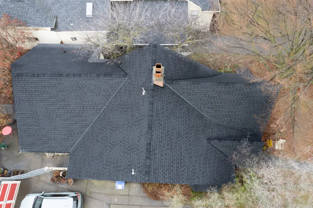 drone shot of black shingle roof surrounded by empty trees