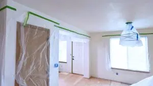 An interior home renovation scene showing rooms prepped with plastic coverings and masking tape.