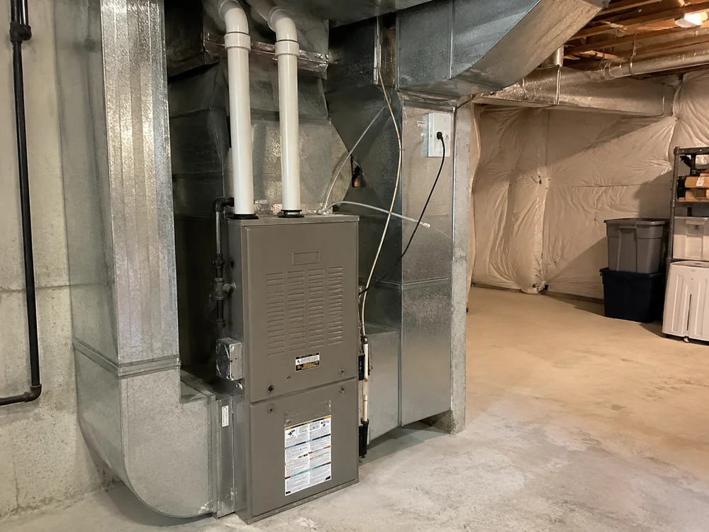 Furnace system installed in a basement with exposed ductwork and visible utility features.