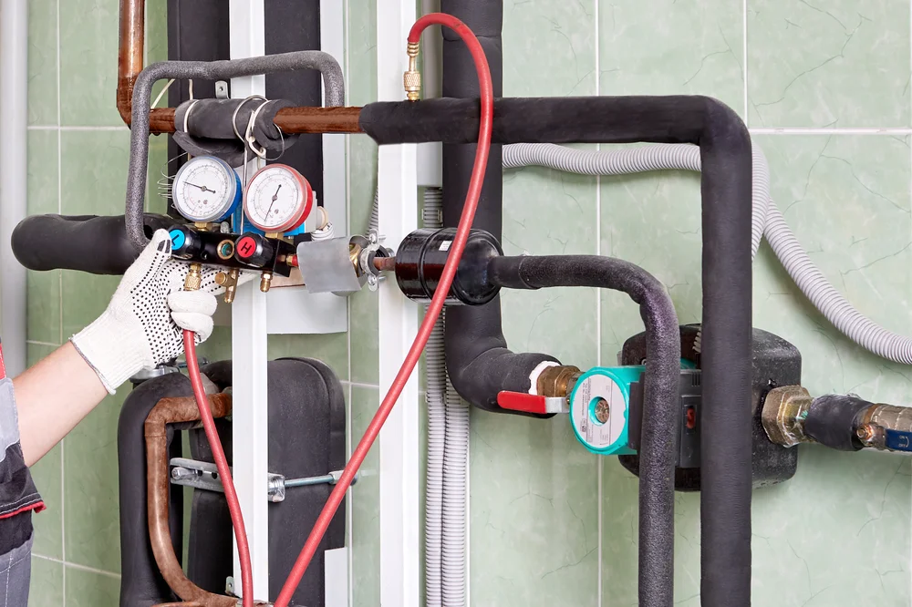 Technician adjusting pressure gauges on HVAC system pipes.