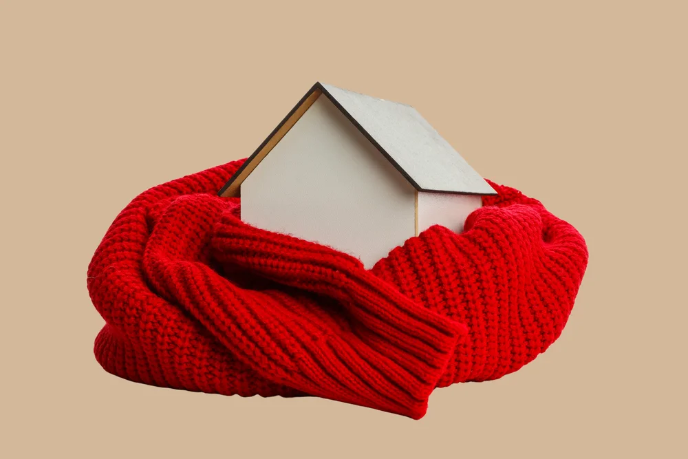 White house figurine wrapped in a red knitted scarf against a beige background.