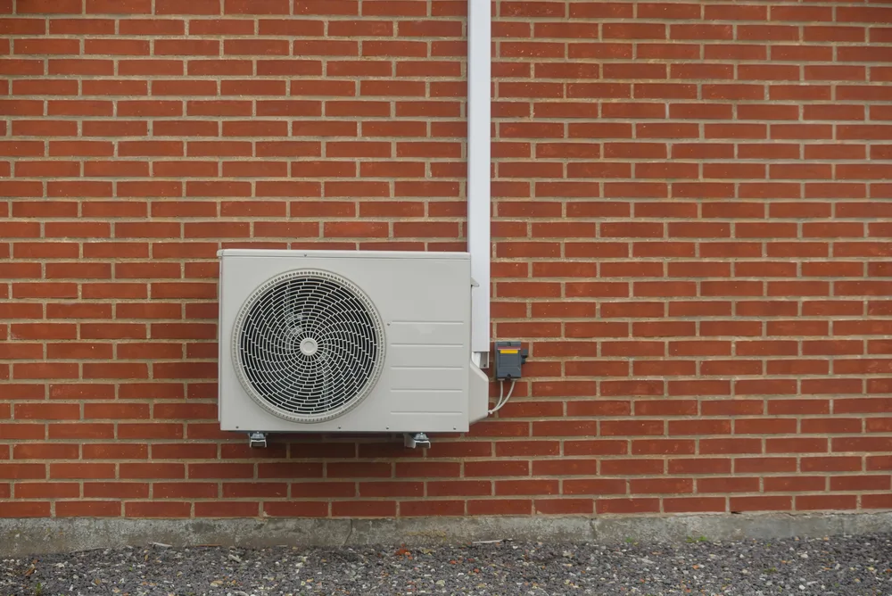 Outdoor air conditioning unit mounted on a red brick wall.