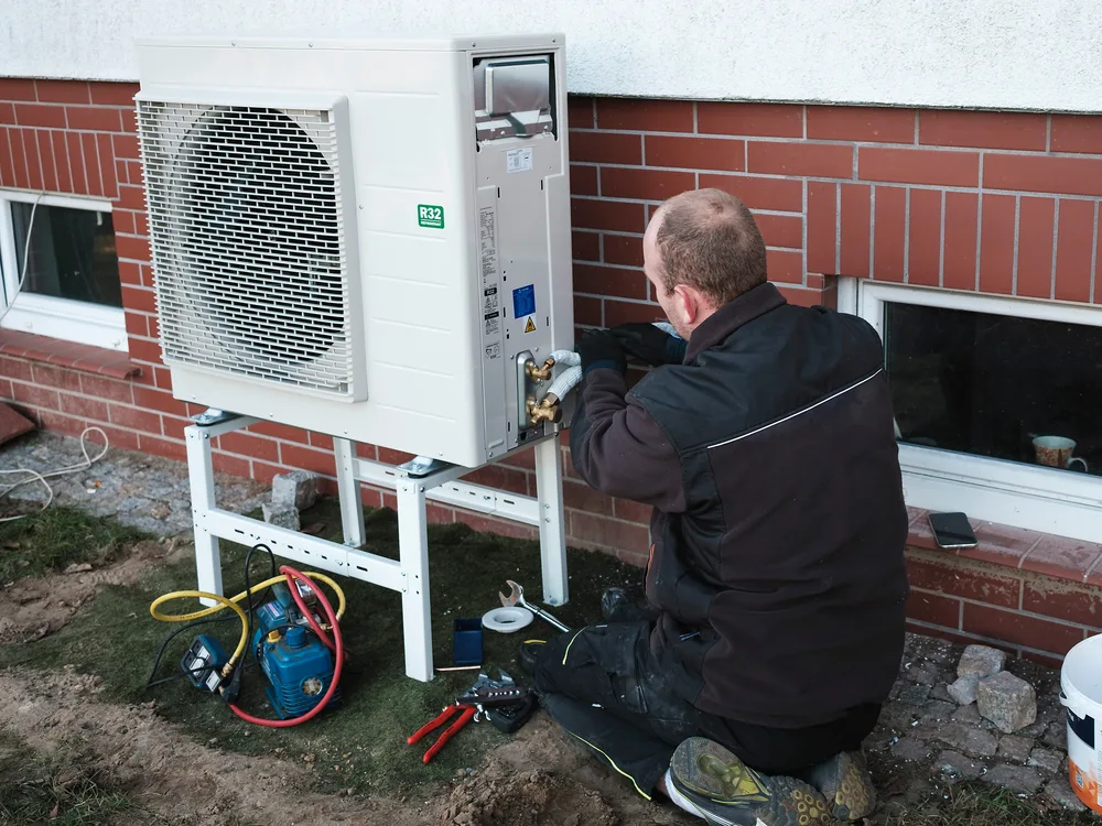 Technician repairing an outdoor air conditioning unit beside a brick building.