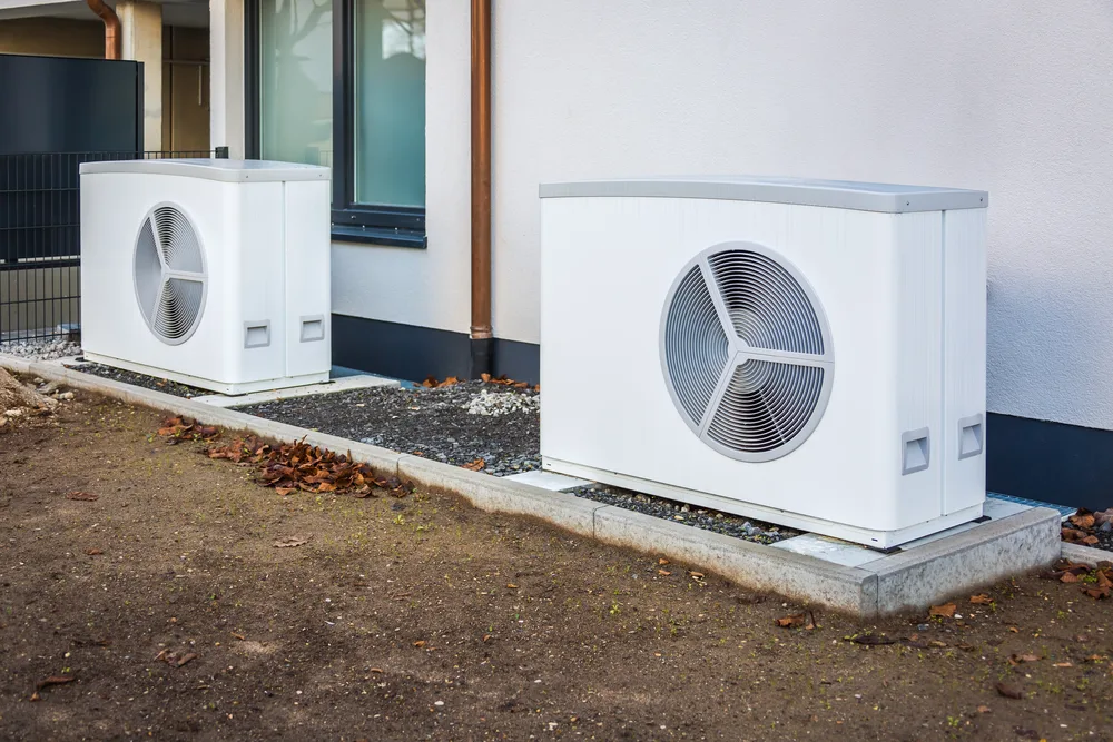 Two large white HVAC units installed on a concrete base outside a building.