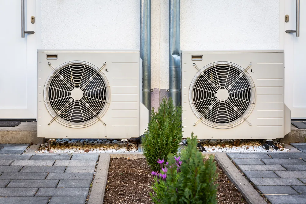 Two outdoor HVAC units installed next to a building with small shrubs in the front.