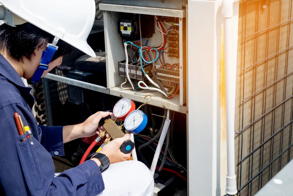 Technician in uniform and hard hat checking HVAC system with gauges.