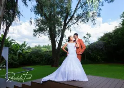 Bride and groom share a joyful moment on the lawn at The Garden Venue wedding venue, under tall trees.