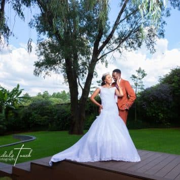 Bride and groom share a joyful moment on the lawn at The Garden Venue wedding venue, under tall trees.