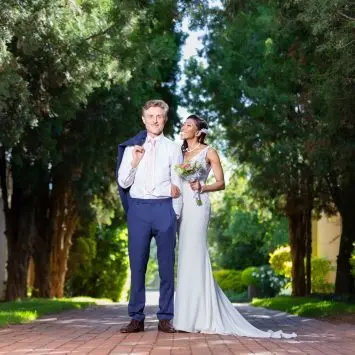 Bride and groom pose playfully on a tree-lined path at The Garden Venue wedding venue, smiling brightly.