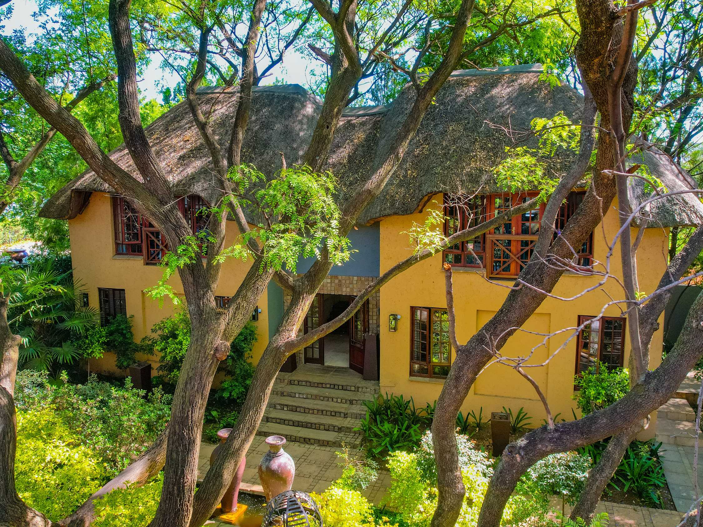 Charming wedding venue building with a thatched roof and yellow walls, surrounded by lush greenery and tall trees, creating a secluded and serene atmosphere.
