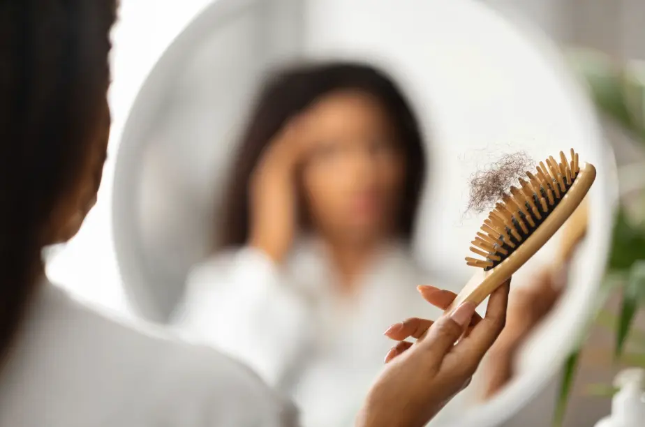 A concerned woman brushing her hair and noticing strands falling out, highlighting the need for hair growth products.