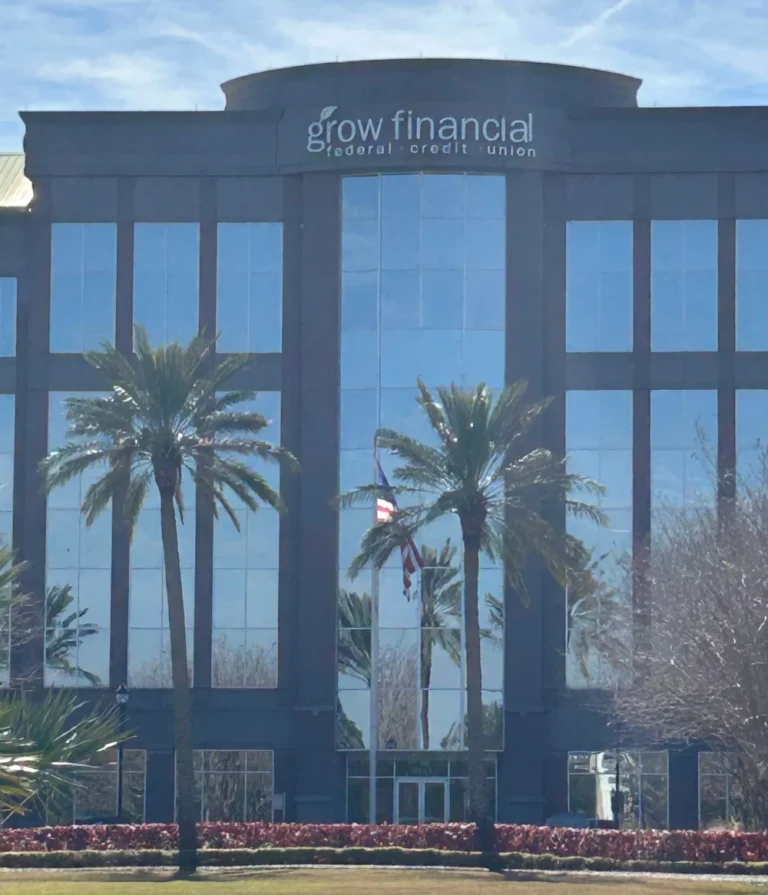 Tall palm trees and manicured red hedges in front of a large glass corporate office building, maintained by commercial landscaping services in Tampa.