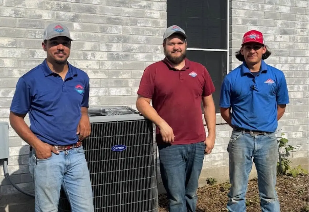 Three team members in front of an AC unit installed outside
