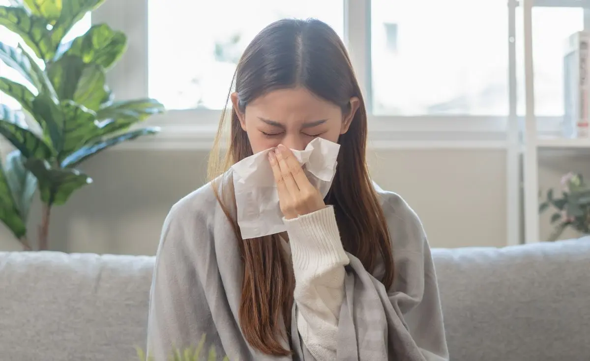 young woman has a common cold and sneezing on the sofa