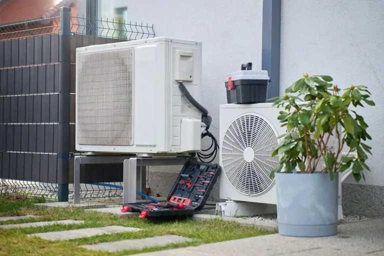 Outdoor heat pump units beside house with open toolbox and tools on ground.