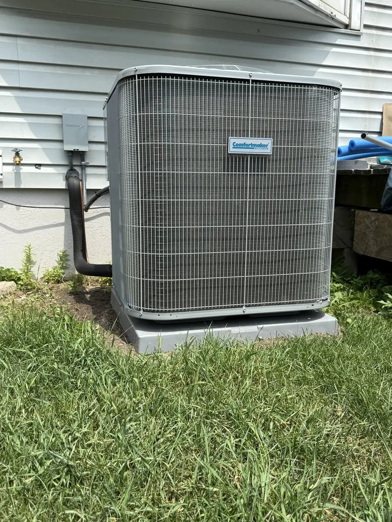 Outdoor air conditioning unit next to a white house, surrounded by green grass.