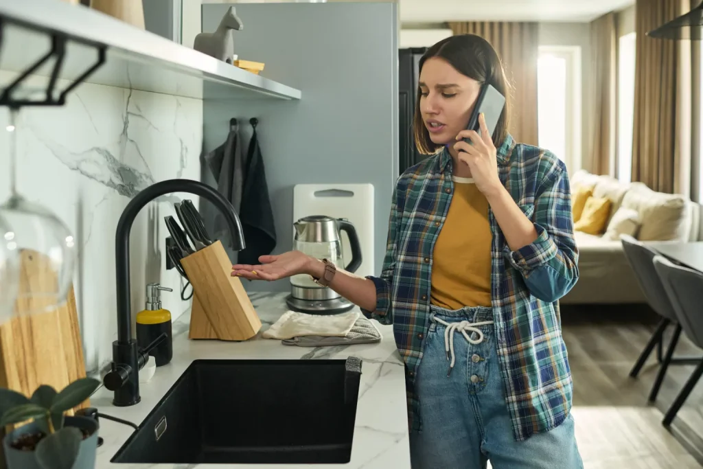Woman having problems with her sink and calling plumber on her cellphone