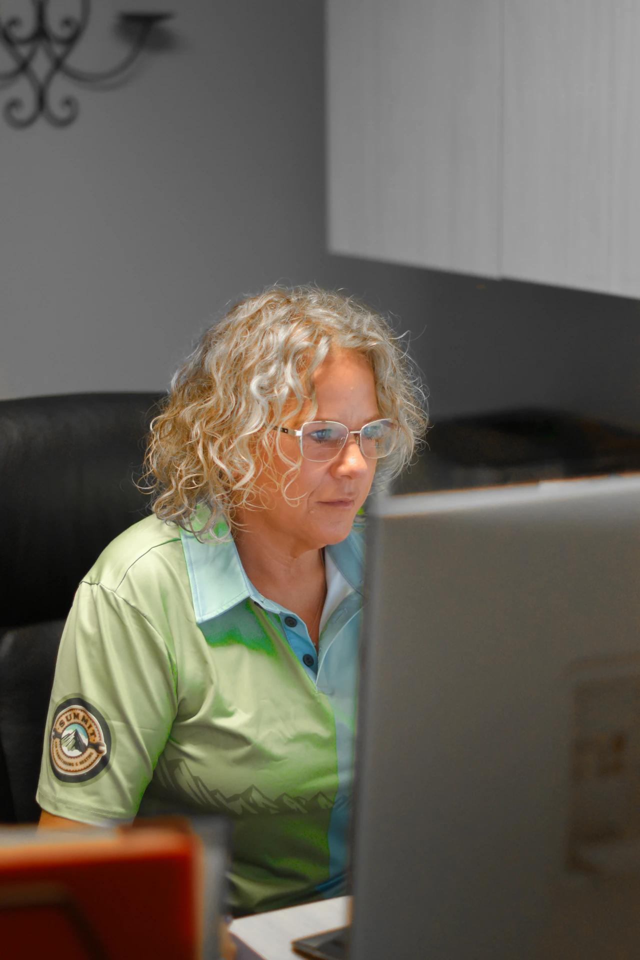 Person with curly hair and glasses focused on a computer screen, wearing a polo shirt with a Summit company logo.
