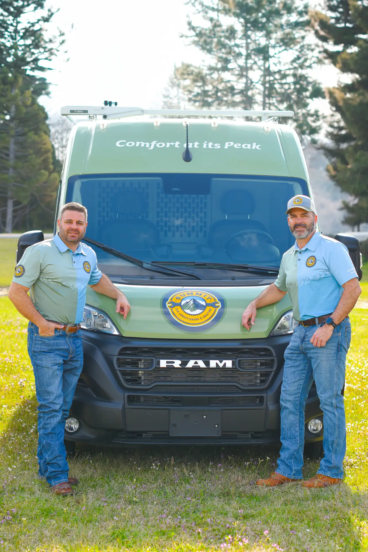 Two men in Summit Air Conditioning & Heating shirts and jeans standing by a green van with "Comfort at its Peak" written on the windshield.