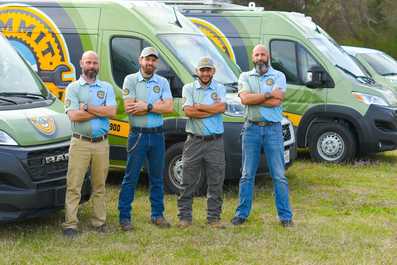 Four men in matching uniforms stand with arms crossed in front of Summit branded service vans.