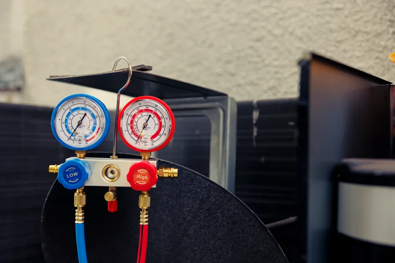 HVAC pressure gauges with blue and red hoses against a neutral background.