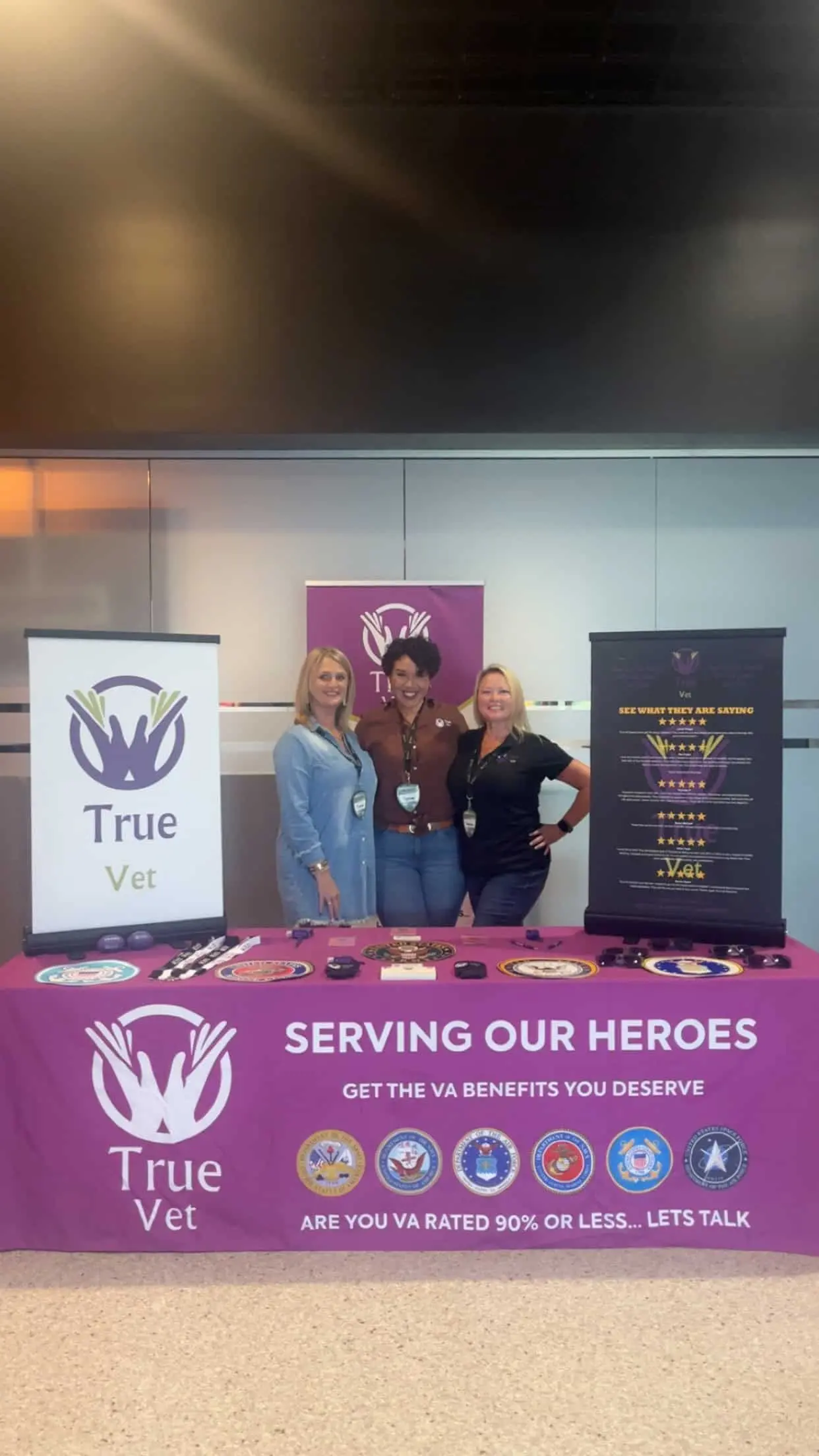Women standing behind a table with "True Vet" branding and promotional materials.