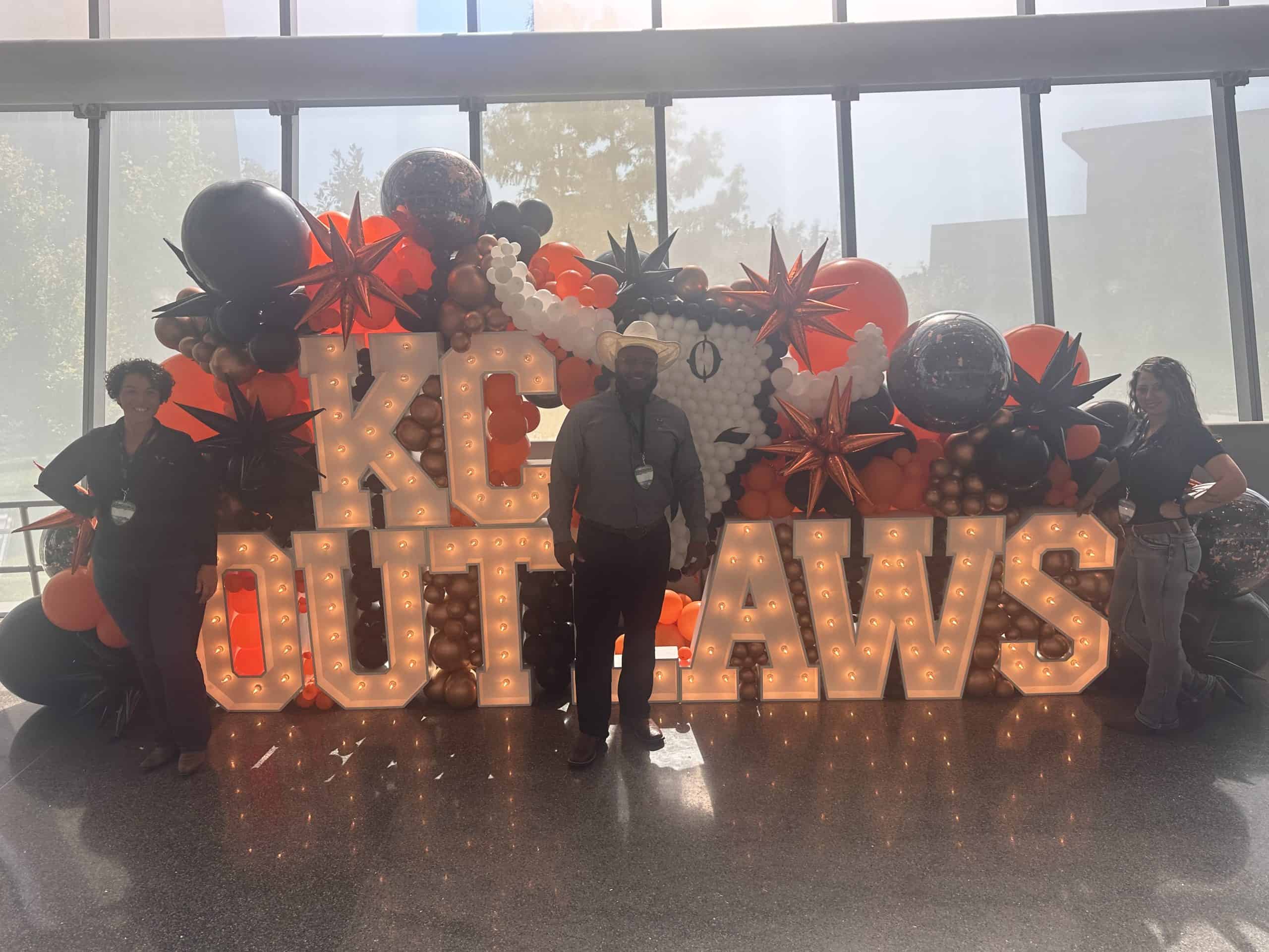 Balloon display with "KID OUTLAWS" sign and people posing.